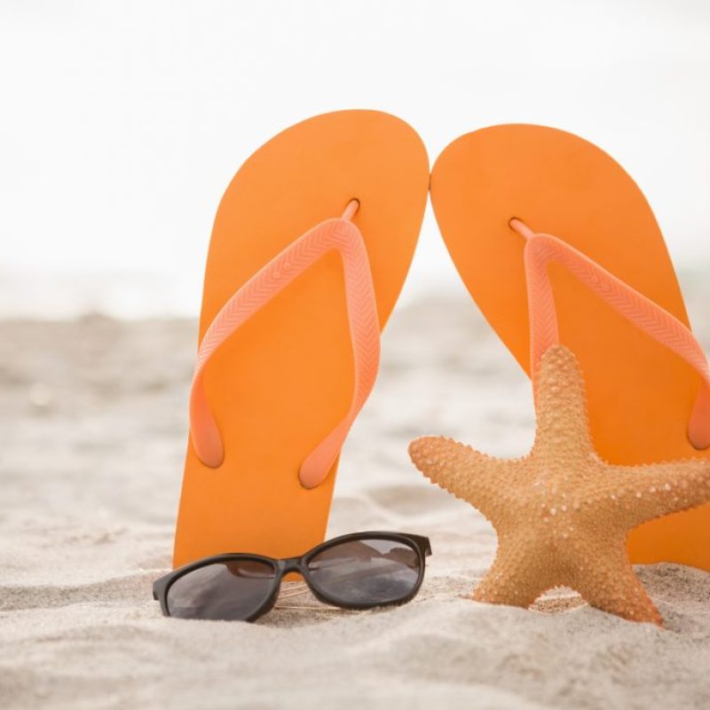 Flip flop, sunglasses and starfish in sand at beach